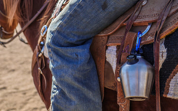 Person on horse back with steel canteen hanging off saddle 