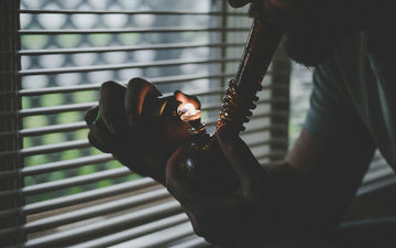 Man smoking softglass bong and blowing smoke out the window