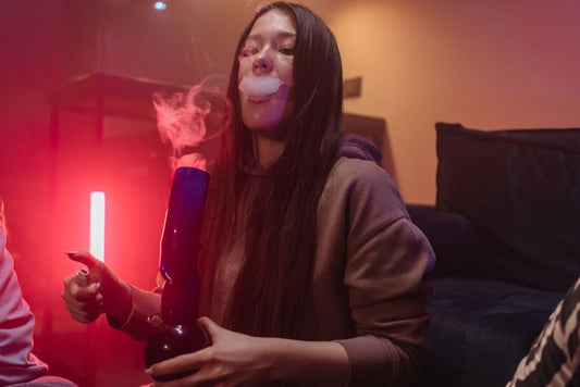 Young woman exhales smoke holding bong
